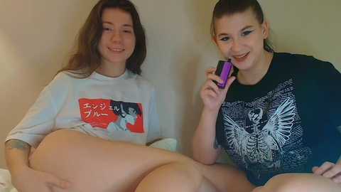 Video of two smiling young women, one with long brown hair in a white t-shirt, the other with dark hair in a black t-shirt with white graphic, holding a purple phone.
