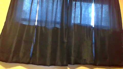 A video of a sheer, dark blue curtain with vertical tassels hanging from a window, partially obscuring a bright light source. The curtain has a textured, slightly translucent fabric.