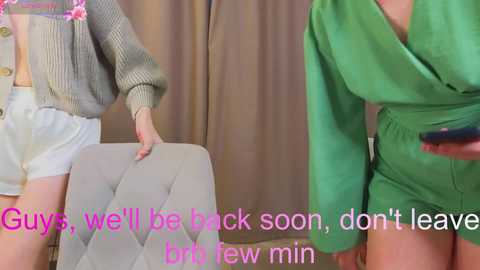 Video of two women in casual attire, one in green, the other in white, standing beside a light gray cushioned chair. Text overlay reads: \"Guys, we'll be back soon, don't leave, brittany few min.\