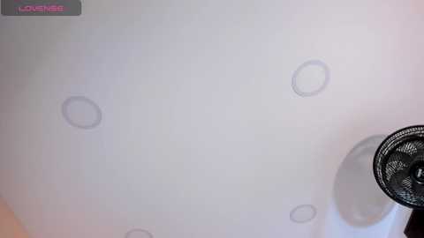 Video of a white ceiling with five faint, circular water stains, a black oscillating fan in the lower right corner, and a \"LOVEWINS\" watermark in the top left corner.