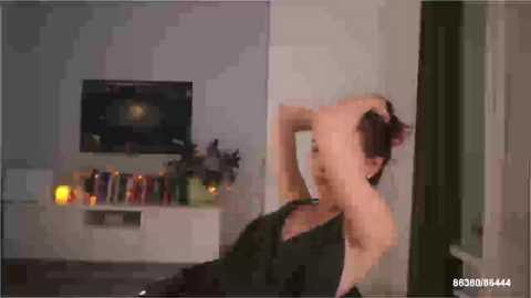 A blurred video of a woman in a dark dress, bending over, with a television and bookshelf in the background.