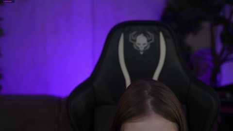 Video of a dimly lit room with a black gaming chair featuring a skull and crossbones logo, purple ambient lighting, and a blurred person in the foreground.