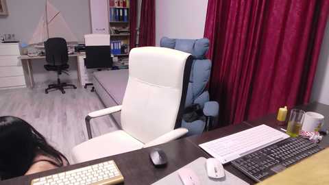 Video of an office with a white leather chair, a computer setup, a keyboard, a mouse, and a glass of water.