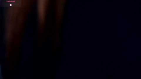 A dimly lit, close-up video of a woman's torso, possibly nude, with skin tones blending into the dark background. The image is grainy and blurry, with minimal details discernible.