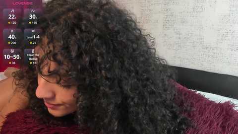 Video of a young Black woman with curly, voluminous black hair, lying on a maroon shag rug against a textured, beige wall. A digital timer displays \"10:50.\
