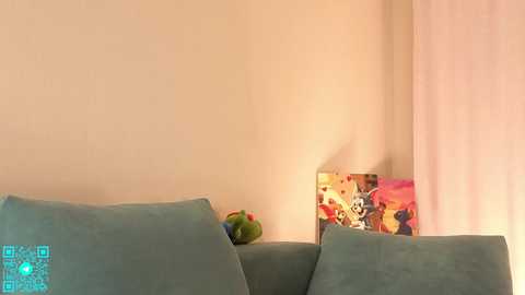A video of a cozy corner featuring a light green couch, a vibrant, colorful painting on the wall, and a small toy on the floor.