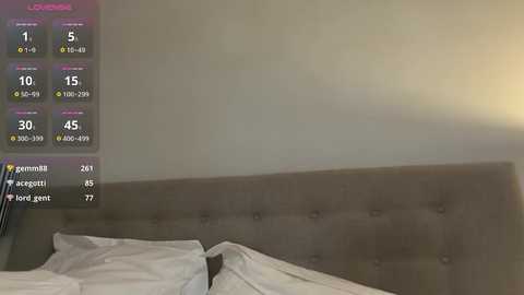 Video of a dimly lit bedroom with a grey upholstered headboard, white pillows, and a partially visible person in bed. A digital overlay displays weather and health metrics.