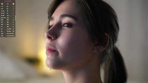 A close-up video of a young woman with fair skin, brown hair, and a tear streaking down her face. The background is blurred, with soft lighting.