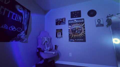 A video of a dimly lit room with a beige chair, a poster of \"Sunshine Superman,\" and various wall art. The ambiance is moody, with blue lighting.