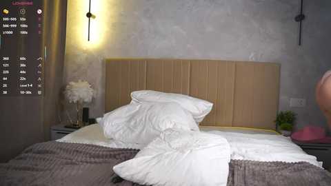 Video of a modern, cozy bedroom with a beige padded headboard, white pillows, and textured grey throw blanket. Minimalist decor, soft lighting, and a digital camera display in the corner.