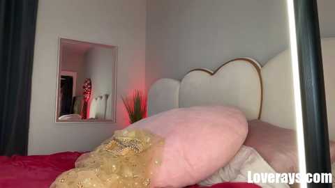 A video of a plush, gold-fabric-clad foot on a red bedspread, with a mirrored wall and a white headboard in a modern bedroom.