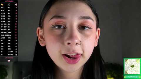 Video of a young woman with light skin, dark hair, and a nose ring, smiling with her tongue out. Background shows a black screen with a \"Loading...\" message.