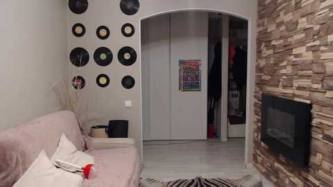 A video of a modern, minimalist living room with a beige couch, stone fireplace, and vinyl records displayed on a white wall.