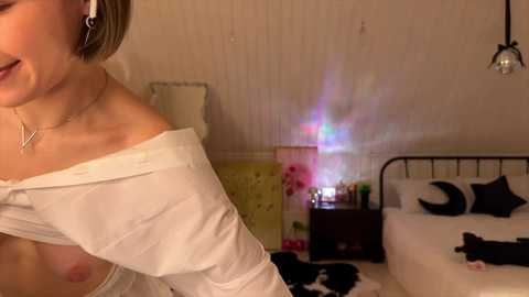 A video of a woman with short brown hair, partially undressed, in a bedroom with a bed, nightstand, and wall art, wearing headphones.