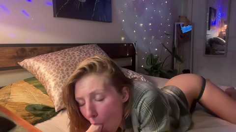 A video shows a blonde woman in an intimate position on a bed, wearing a green sweater and black thong, her face in a sexual expression.
