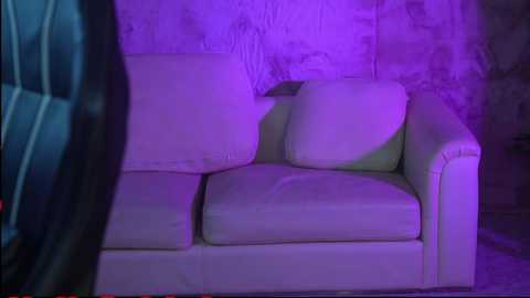 A video of a dimly lit, white leather sofa with purple lighting, set against a textured, light gray wall. The background is blurred, giving a mysterious, slightly eerie ambiance.