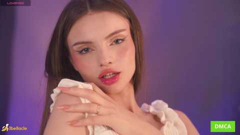 A close-up video of a young, fair-skinned woman with long, straight brown hair, wearing a white, ruffled dress, looking pensive with pink lipstick. Background is a blurred purple gradient.
