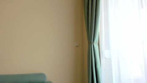 Video of a minimalist room with a beige wall, a light blue curtain, and a white light switch on the left. A soft light filters through the curtain, creating a serene atmosphere.