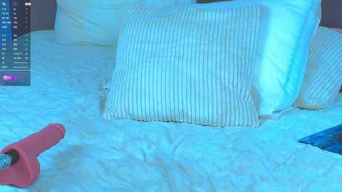A video of a bed with white bedding, including a pillow with vertical stripes, a pink shoe, and a blue piece of clothing on the floor, bathed in soft blue light.
