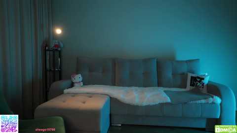 Video of a dimly lit, minimalist bedroom with a plush grey couch, white blanket, and a plush Hello Kitty toy.