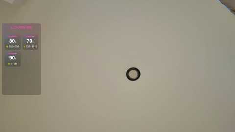 Video of a white wall with a small, black circular sensor in the center. To the left, a digital thermometer display shows temperature readings in Celsius and Fahrenheit. The background is plain and uncluttered.