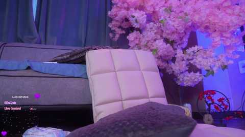 Video of a modern living room with a gray sofa, white cushioned chair, and a cherry blossom tree in the background.