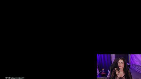 Video featuring a woman with long, dark hair and a black lace top, standing against a black backdrop. A smaller inset shows a man in the background, with purple lighting.