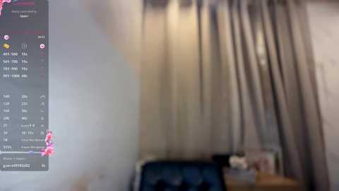 A blurry video of a beige curtain with a dark pattern, possibly a door, and a calendar with pink flowers on the left. The background is indistinct, likely a room with furniture.