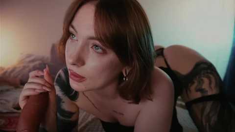 Video of a fair-skinned, red-haired woman with blue eyes, wearing black lingerie, lying on a bed with a tattooed man's erect penis in her hand.