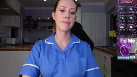 Video of a Caucasian woman with light skin and brown hair, wearing a blue scrub top, standing in a modern kitchen. The image overlays a fitness app screen with health data.