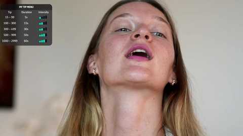 Video of a Caucasian woman with fair skin, long blonde hair, and pink lipstick, wearing small gold earrings, mid-sentence, in an indoor setting.