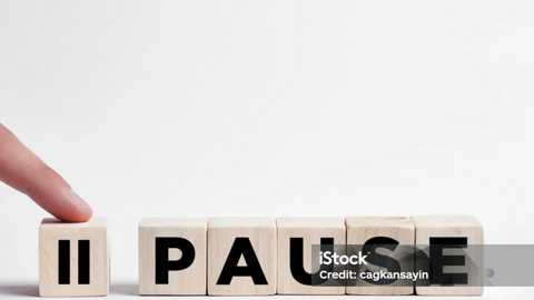 Video of a person's hand placing a wooden letter \"U\" into the word \"PAUSE\" made from wooden blocks. The background is plain white, emphasizing the wooden letters and hand.