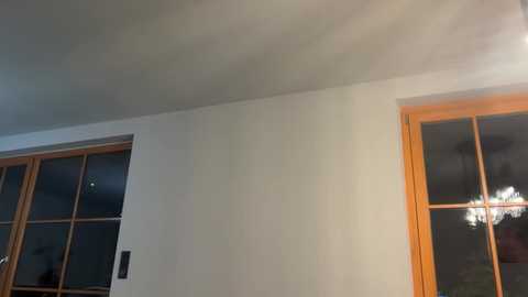 Video of a dimly lit room with a white wall and two wooden-framed windows. One window has a black sensor, casting a shadow. The ceiling is slightly visible, indicating a low angle shot.