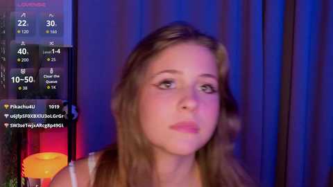 Video of a fair-skinned, light-haired woman in a white top, looking thoughtful against a dark curtain backdrop. A digital display shows temperature, humidity, and air quality data.