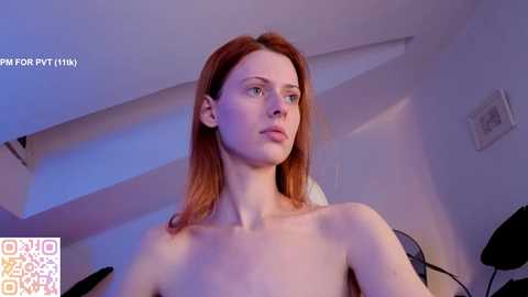 Video of a fair-skinned, red-haired woman with small breasts, standing topless in a dimly lit, modern room with a ceiling fan and abstract art on the wall.