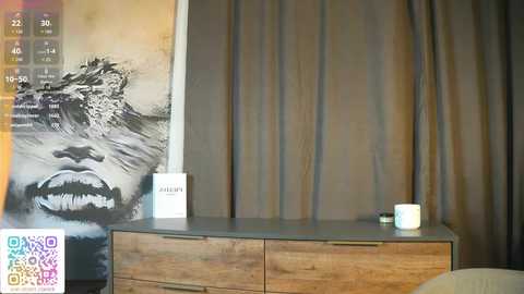 Video of a minimalist room with a wooden dresser, a white Armani bottle, and a white cup on a grey countertop. A large, black-and-white video of a lion's face covers a wall, and beige curtains hang behind.
