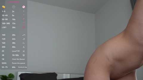 A video of a nude, light-skinned woman with a slender figure, viewed from the side. She stands in a modern, minimalist bedroom with white walls and a black headboard. A digital interface with health data is overlaid on the left.