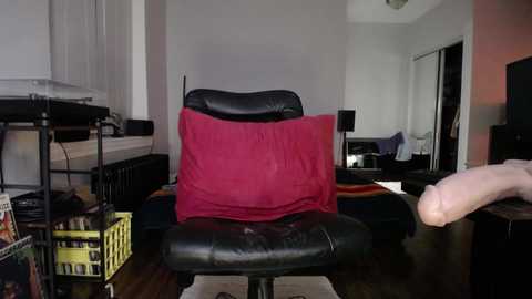 A video depicts a cozy, lived-in living room with a black leather recliner, a red throw blanket, a yellow laundry basket, and a TV on a wooden stand.