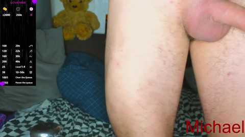 A video of a naked man's penis and testicles, with a yellow teddy bear in the background. The image features a digital overlay with metrics and the username \"Michael\" in red.