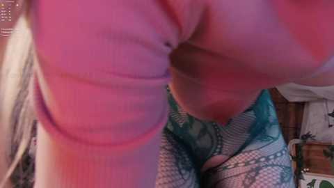Video of a woman with fair skin, wearing a pink top and turquoise leggings, bending over in a dimly lit room, focusing on her buttocks and thighs.