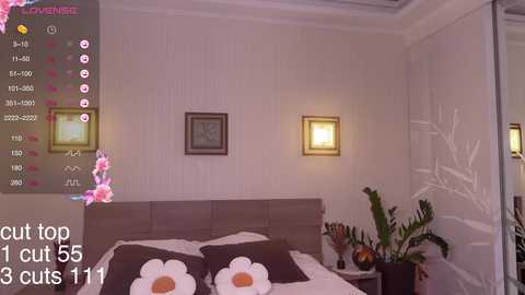 A video of a modern, minimalist bedroom with a beige headboard, floral pillowcases, a white nightstand with a potted plant, and a framed picture on the wall.