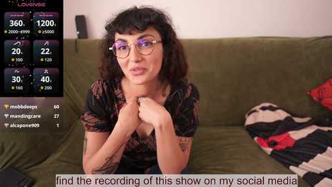 A video of a middle-aged woman with curly hair, wearing glasses, and a colorful dress, sitting on a green couch, with a live stream overlay showing social media likes and comments.