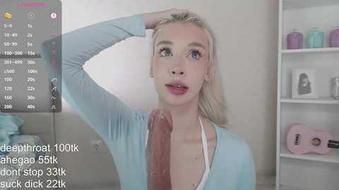 A video of a blonde woman with fair skin and blue eyes, wearing a light blue top, standing in a modern bathroom.