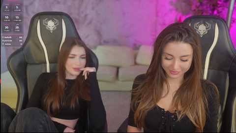 Video of a young woman with long brown hair, wearing a black crop top, sitting on a gaming chair, with a blurred background of a living room.