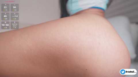 Video of a close-up of a person's bare buttocks, with a blurred background showing a person wearing a mask and a blue top, and a digital timer in the top left corner.