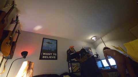 A video of a cluttered, dimly-lit bedroom featuring a poster of a UFO, a guitar, and various electronic devices.