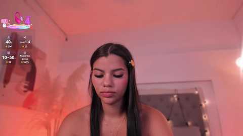 A video of a young, light-skinned woman with long black hair, wearing a gold hair clip, standing in a dimly lit, pink-lit room. The image includes a digital overlay with a countdown clock.