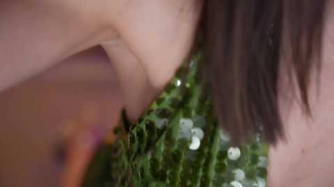 Video: Close-up of a woman's bare shoulder with a green sequin dress, focusing on the intricate sequin texture and her dark hair.