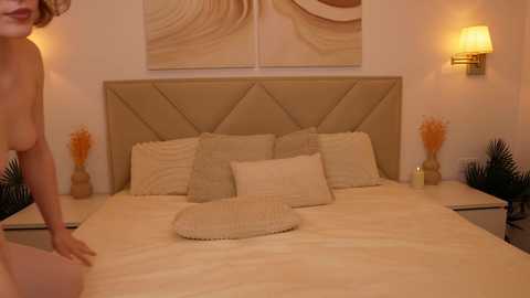 A video of a beige-tiled bathroom with a large, cushioned bed, two bedside tables, and a wall-mounted lamp.