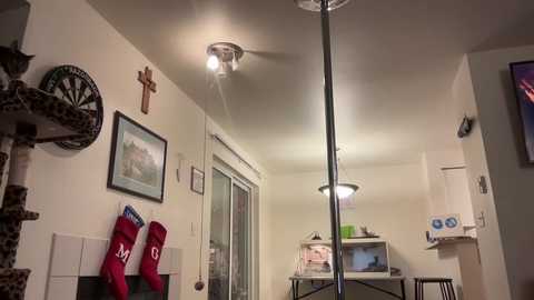 Video of a cozy, cluttered living room with a ceiling fan, a crucifix, framed art, Christmas stockings, and a small bookshelf.